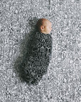 A baby swaddled laying on top of the quilt spread out