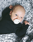 A baby with a binky laying on the quilt