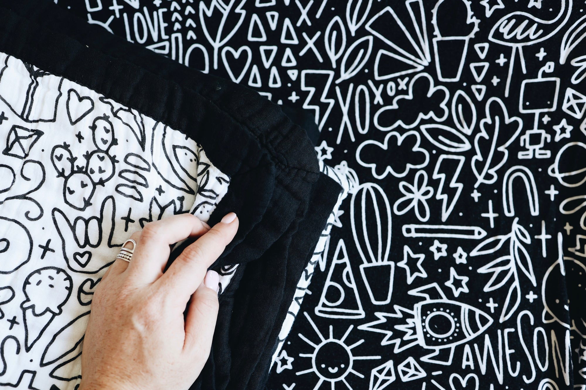 A hand holding the corners of the folded quilt on a doodled background