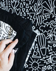 A hand holding the corners of the folded quilt on a doodled background