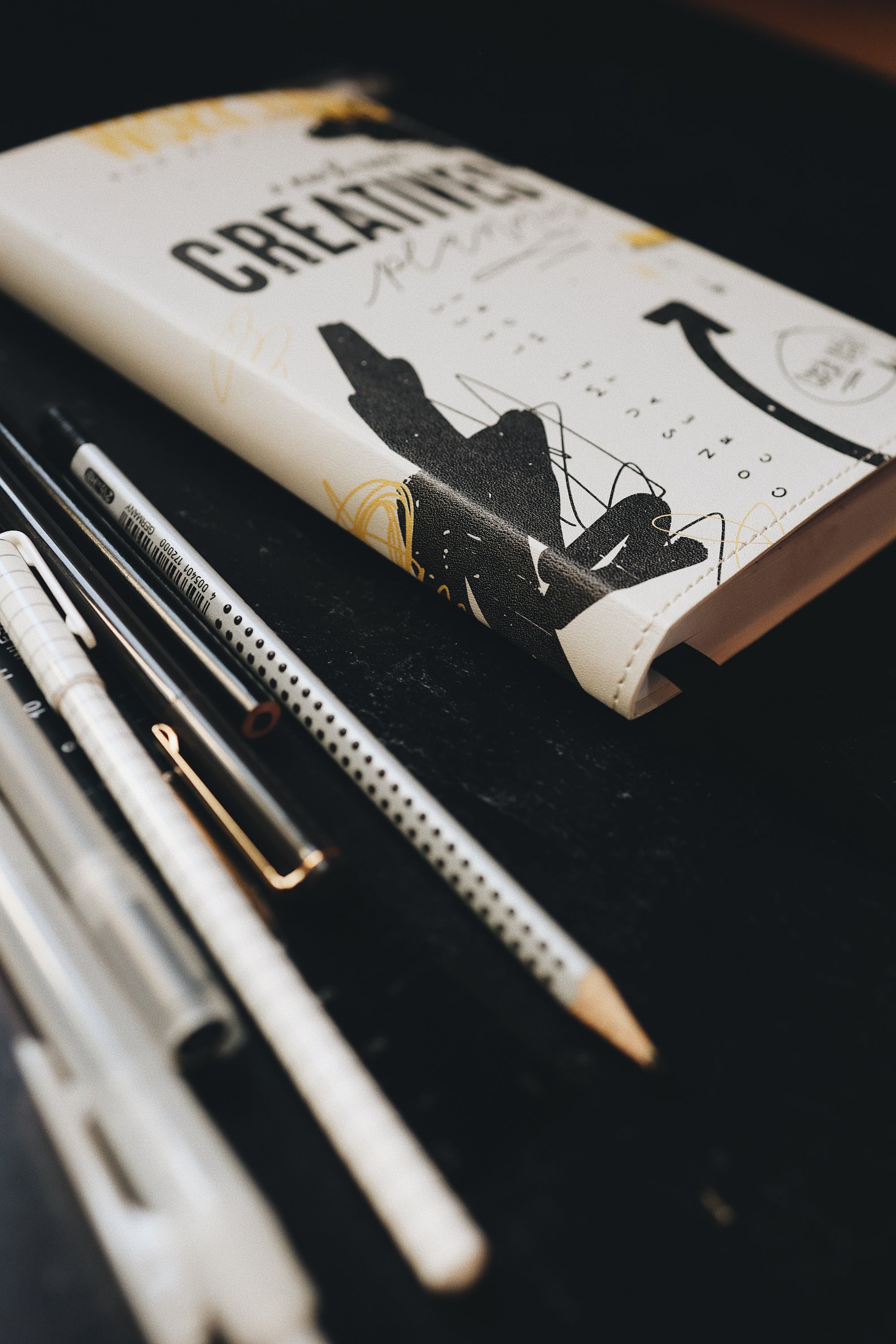 Artistic shot of the binding of the planner, sitting on a desk alongside some pens
