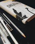 Artistic shot of the binding of the planner, sitting on a desk alongside some pens
