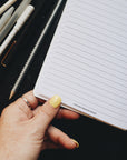Thumb holding the creative planner open to the project page, artistic shot at an angle