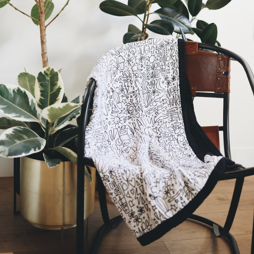 The quilt draped over a chair with houseplants in the background