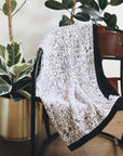 The quilt draped over a chair with houseplants in the background