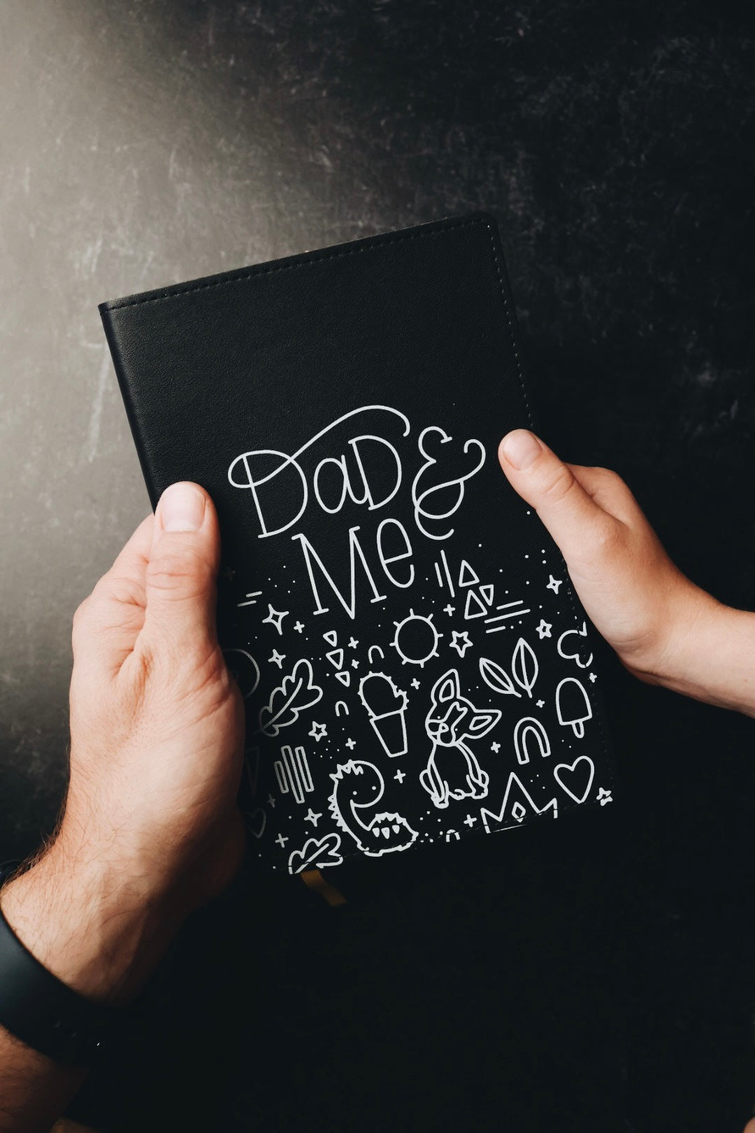 Two hands holding dad & me journal showing cover