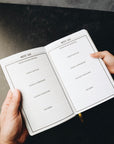 Two hands holding journal open to prompts page