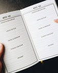 Two hands holding journal open to prompts page
