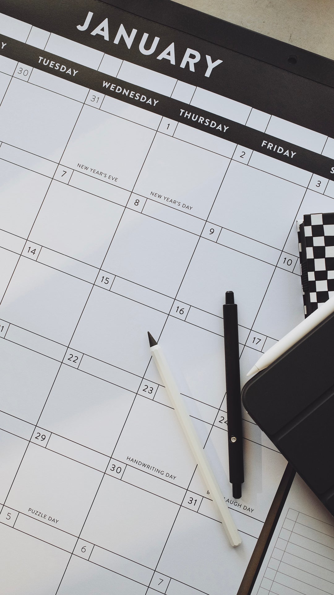 Pens and planners laying on top of a calendar showing the month of January on a light gray surface