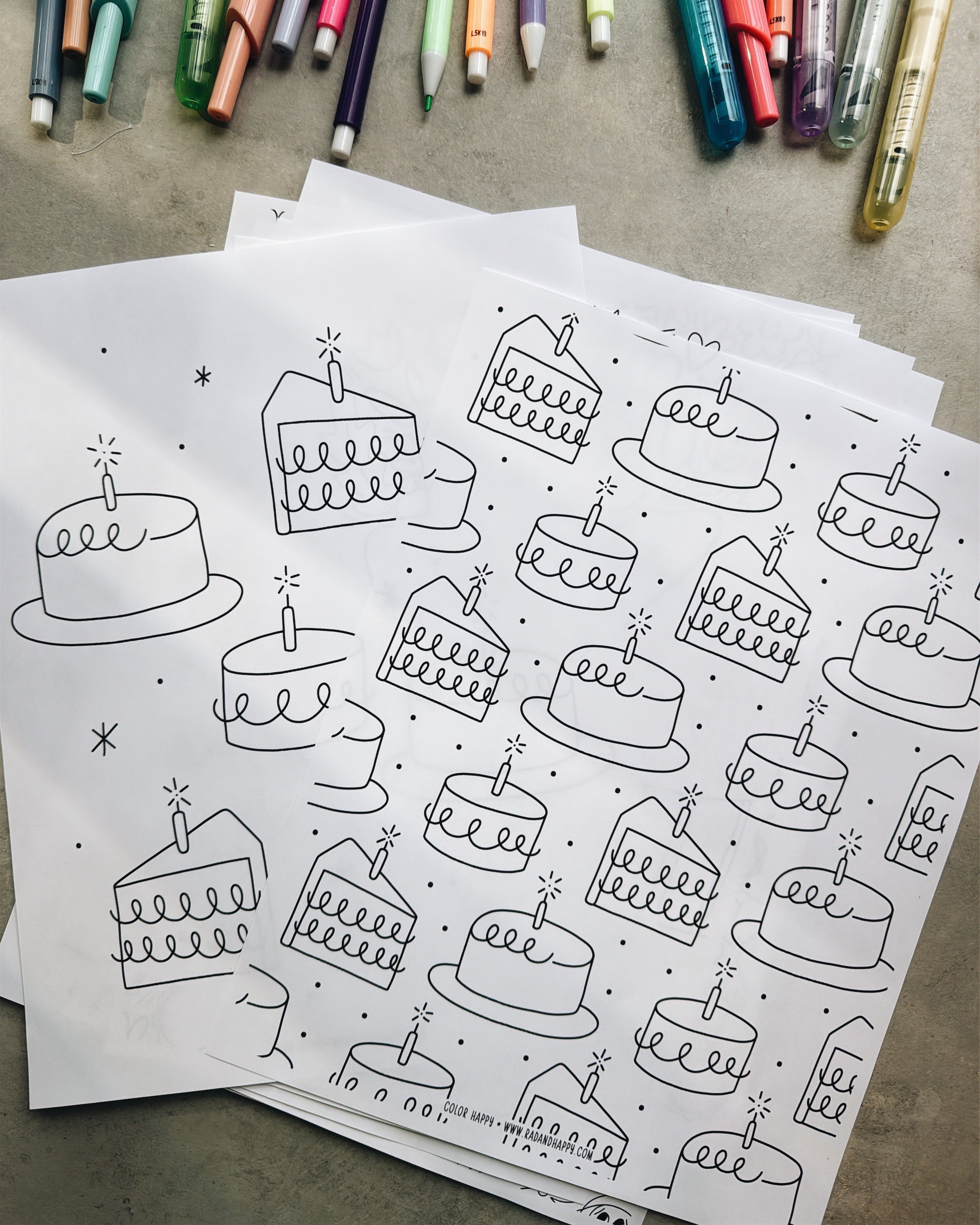 Pages of cake illustrations on paper with markers in the background