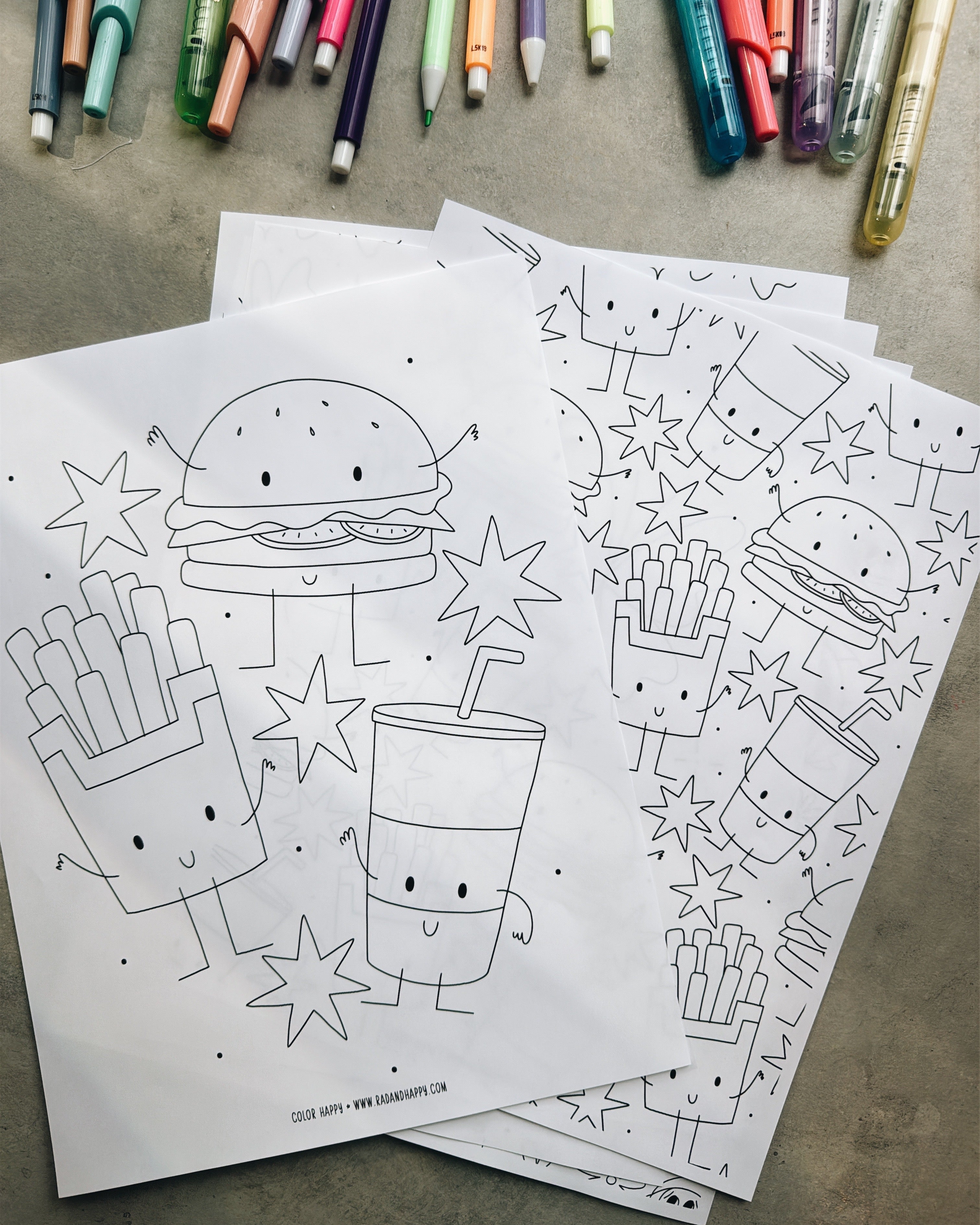 Coloring pages with cartoon food characters on a concrete surface with markers.