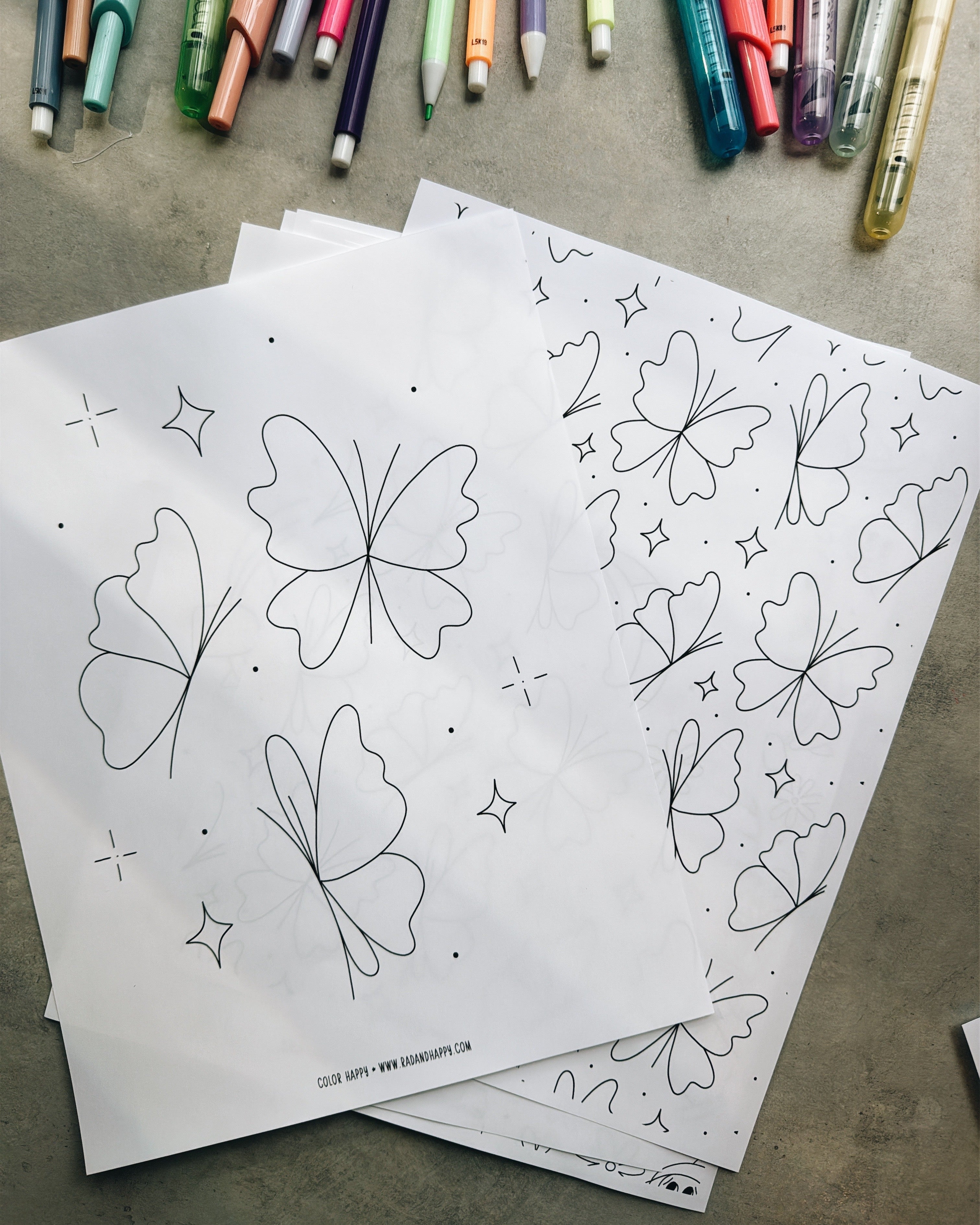 Butterfly and flower outlines on paper with colorful markers on a gray surface