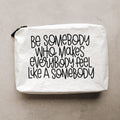A white Tyvek zipper pouch with the text 'BE SOMEBODY WHO MAKES EVERYBODY FEEL LIKE A SOMEBODY' written in black.