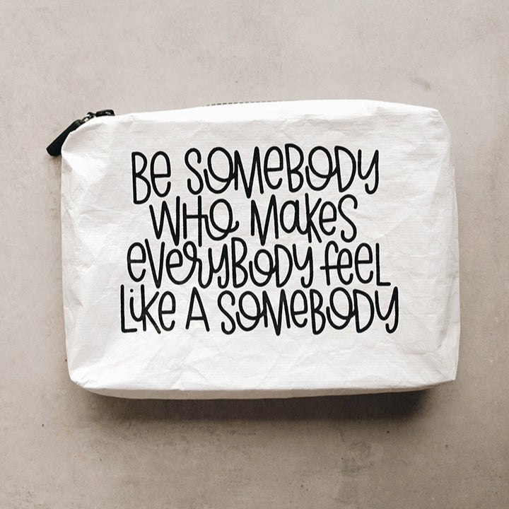 A white Tyvek zipper pouch with the text 'BE SOMEBODY WHO MAKES EVERYBODY FEEL LIKE A SOMEBODY' written in black.