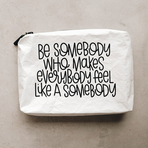 A white Tyvek zipper pouch with the text 'BE SOMEBODY WHO MAKES EVERYBODY FEEL LIKE A SOMEBODY' written in black.