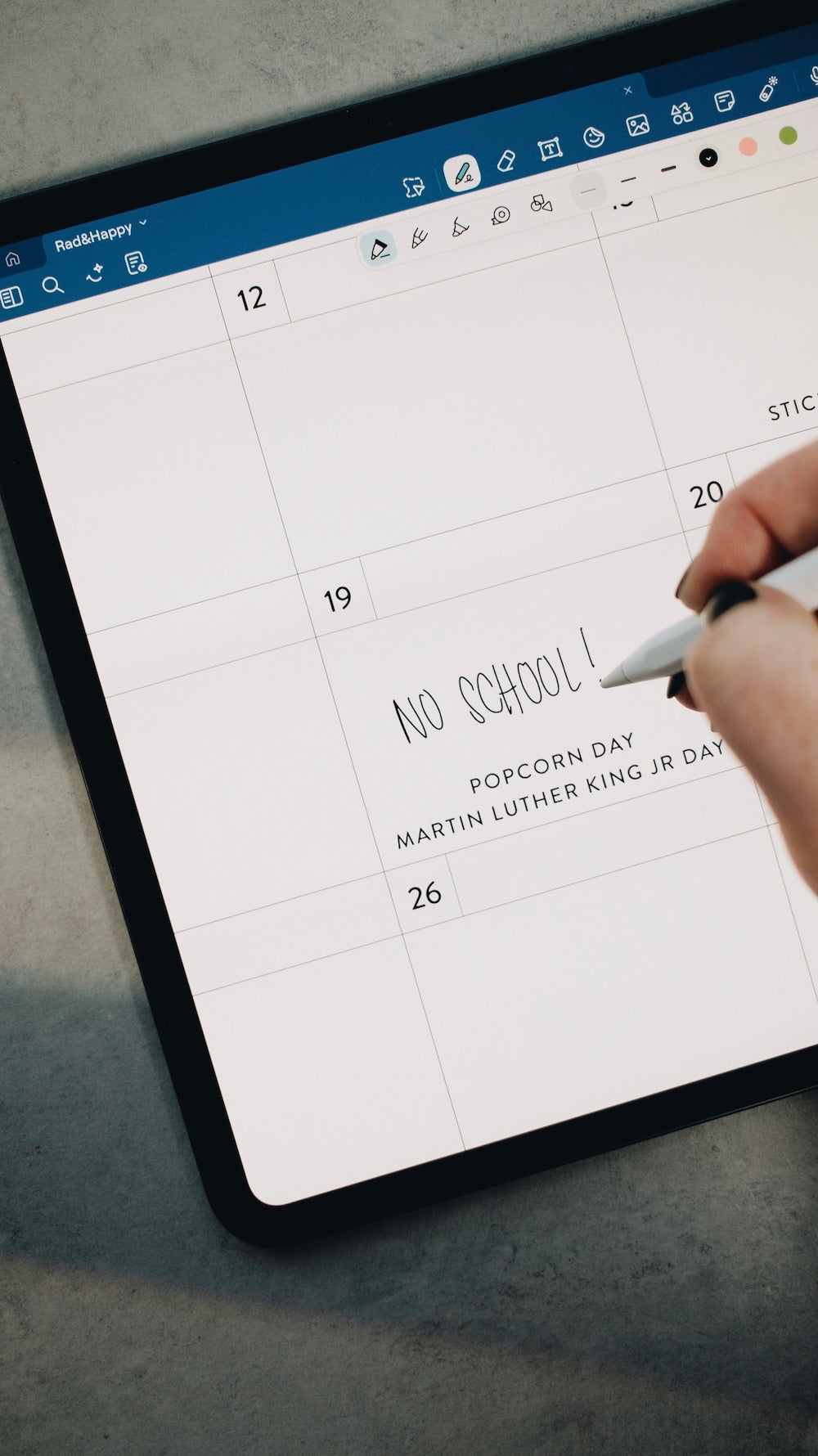 Hand using a stylus to write on a digital planner in the Goodnotes app on a tablet.