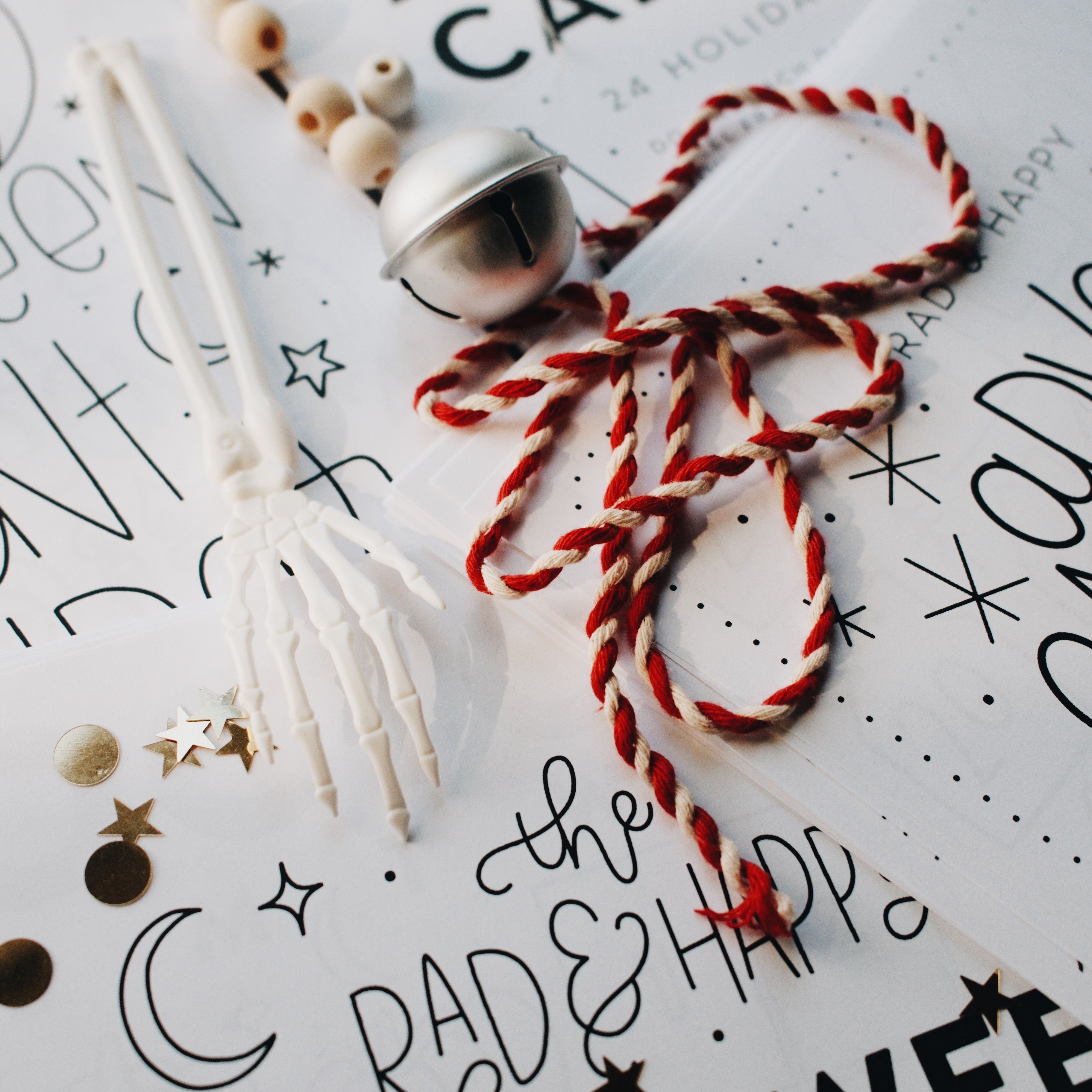 Silver bell with a red and white string and a plastic skeleton hand on top of advent paper