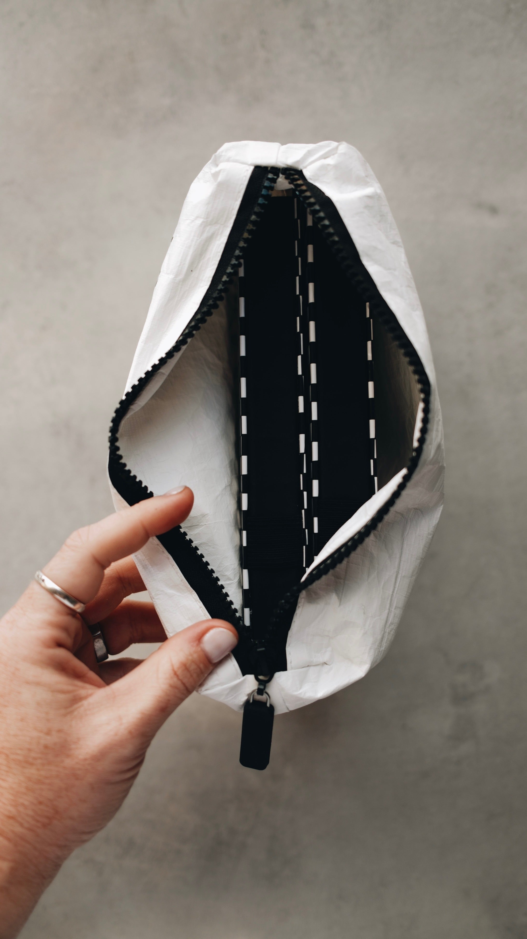 Top view of the white tyvek zipper pouch with the zipper open and a hand holding the zipper and sketchbooks inside