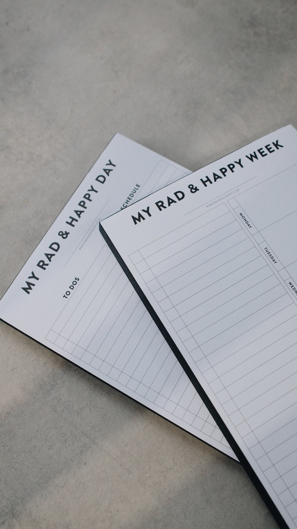 Two notepads stacked with the text "My Rad & Happy Week" on a gray surface