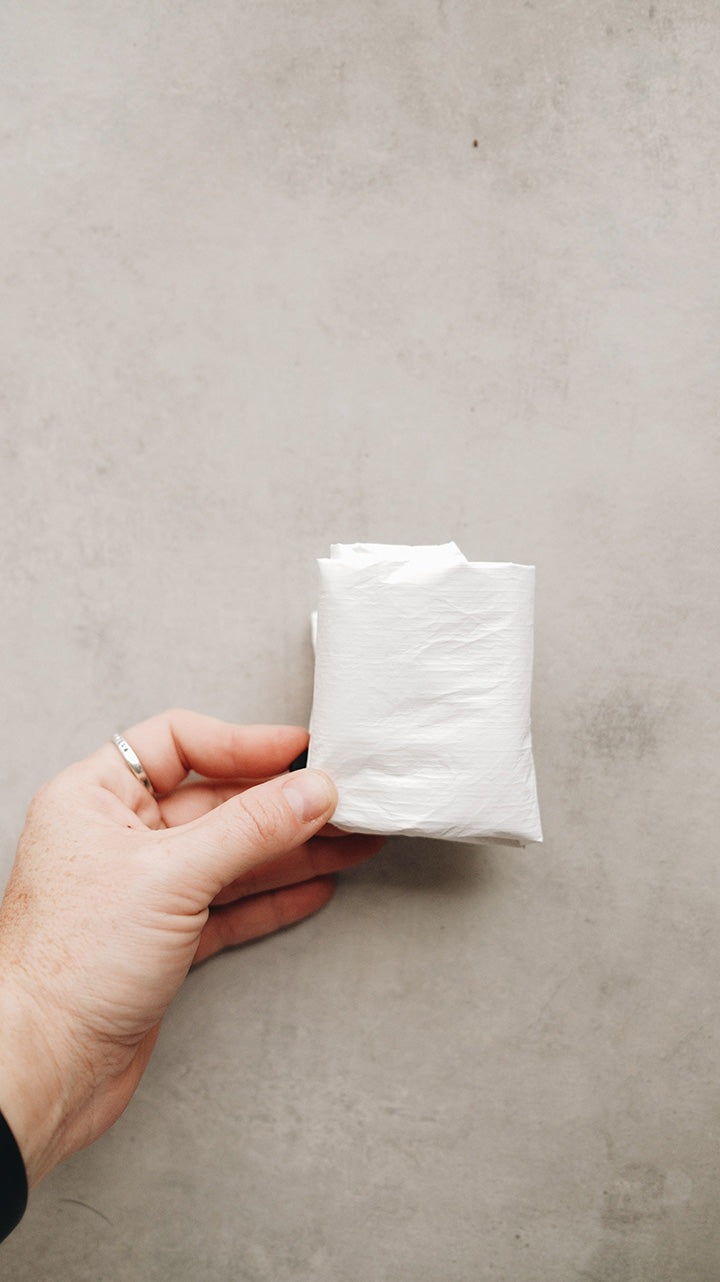 A hand holding a white tyvek zipper pouch folded up into a neat little square with a gray surface in the background