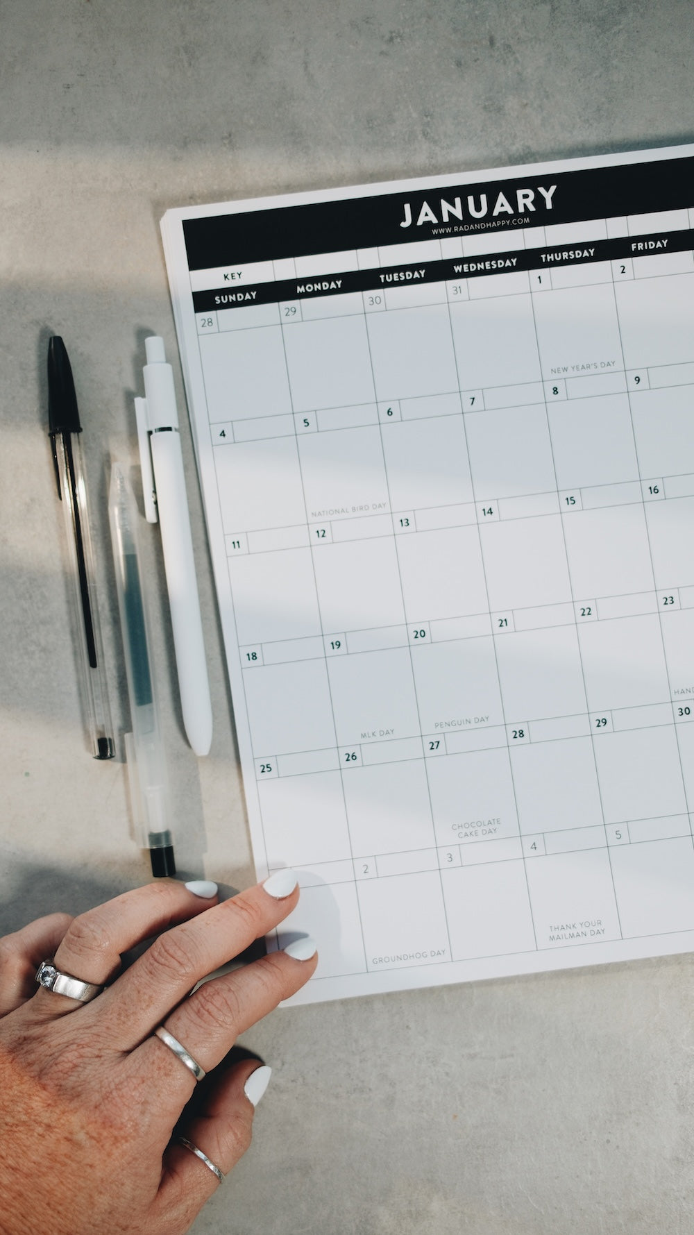 Calendar for January with a hand resting nearby with pens on a gray surface