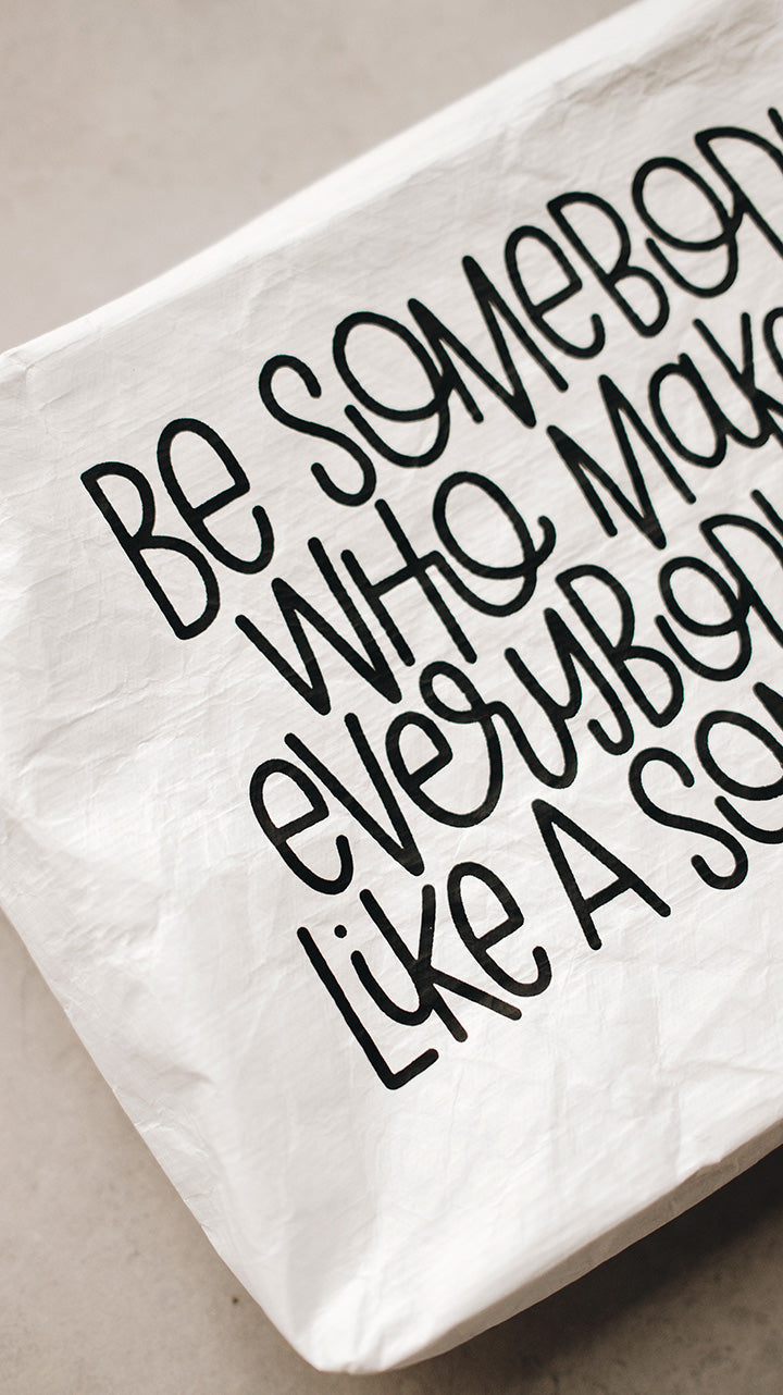 White tyvek zipper pouch zoomed in on the text be somebody who makes everybody feel like a somebody in black text
