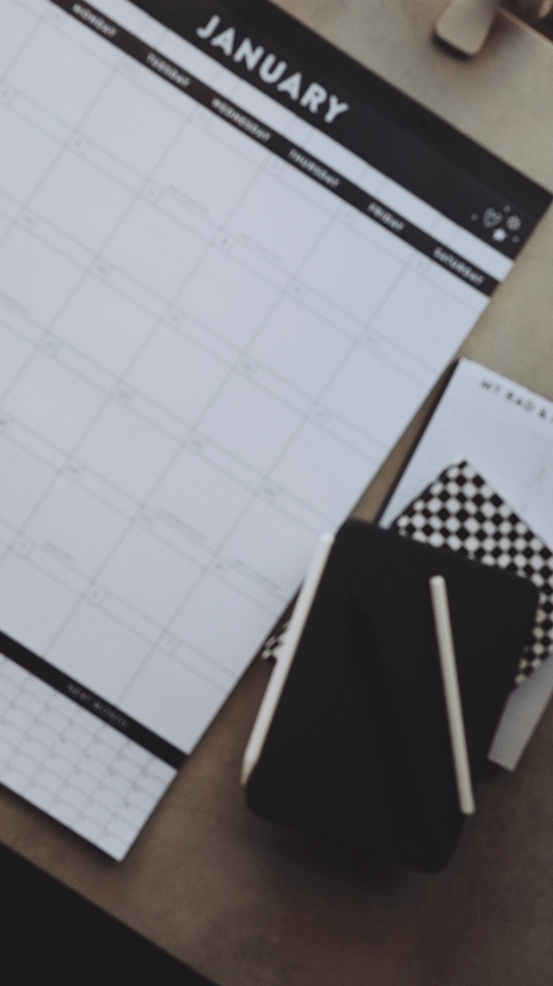 January calendar page sitting next to a stack of planners and a pen laying on a light gray surface 