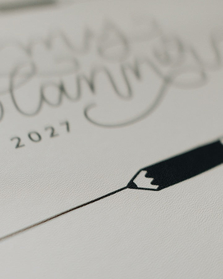 A close-up of a white textured planner page featuring elegant black cursive writing that reads 'my planning 2027' and a minimalist black pencil illustration.