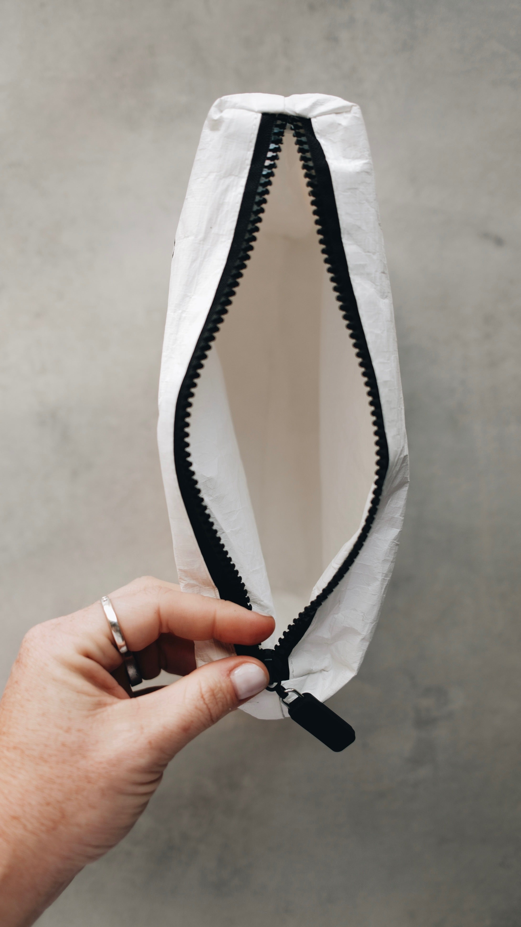 Top view of the white tyvek zipper pouch with the zipper open and a hand holding the zipper