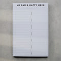 Weekly planner pad titled 'My Rad & Happy Week' on a gray surface