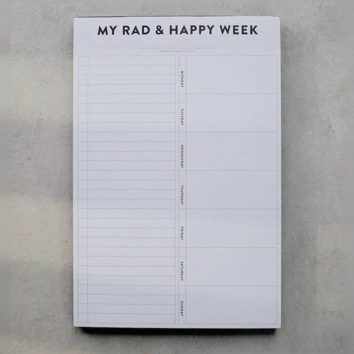 Weekly planner pad titled 'My Rad & Happy Week' on a gray surface