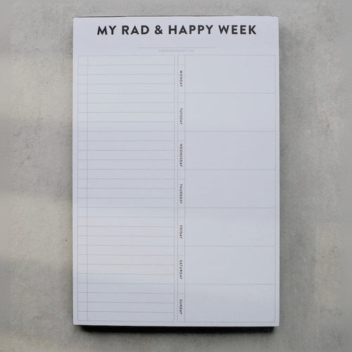 Weekly planner pad titled 'My Rad & Happy Week' on a gray surface
