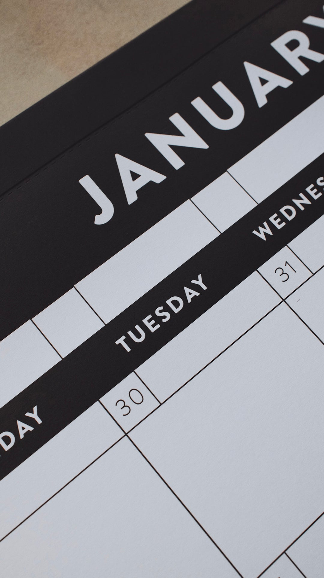 A close-up picture of a January calendar with a focus on the word "Tuesday" in white letters with a black background