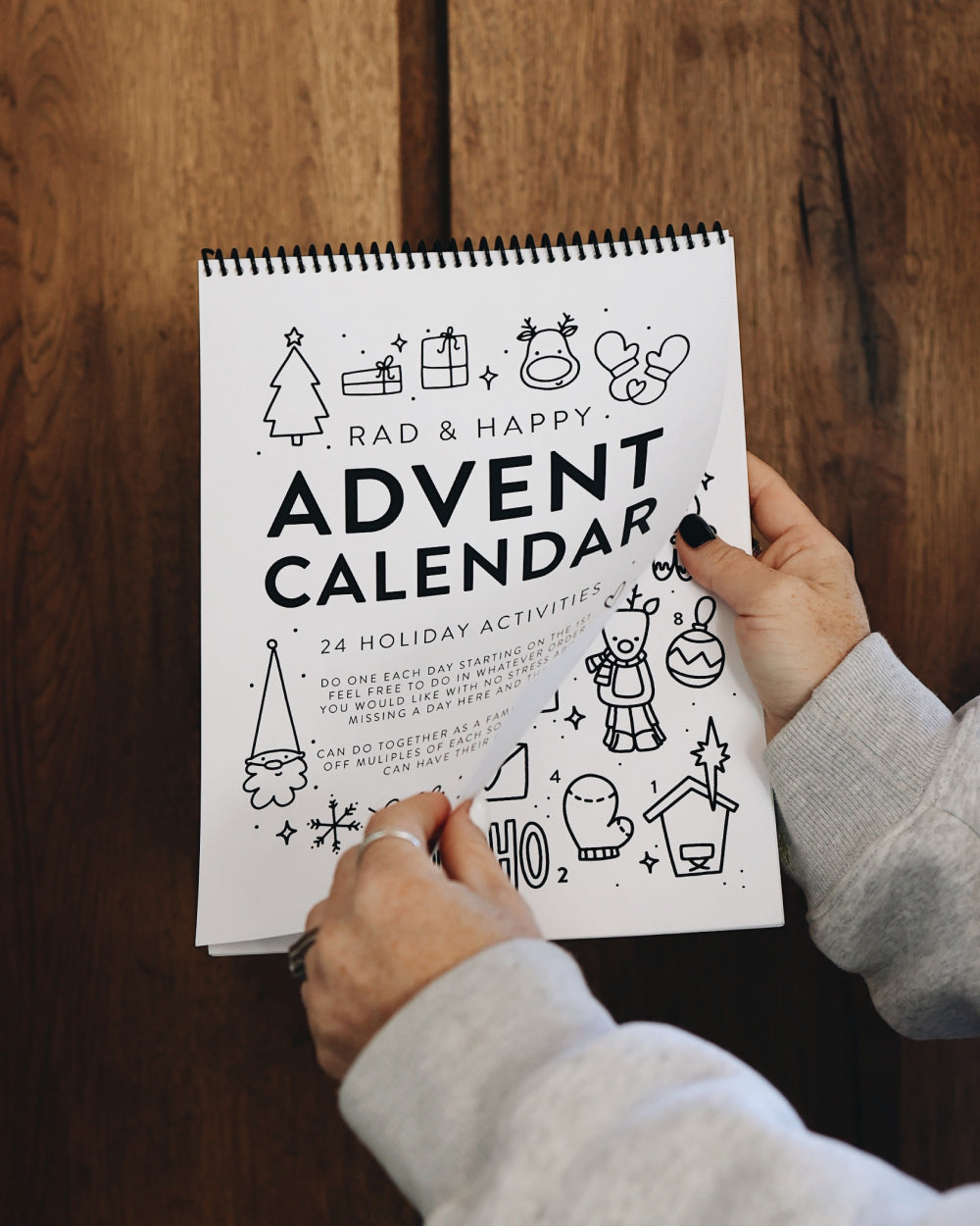 Person holding a spiral-bound Advent calendar with black and white illustrations on a wooden surface