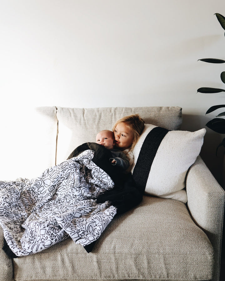 A child snuggling a baby on a couch under the quilt