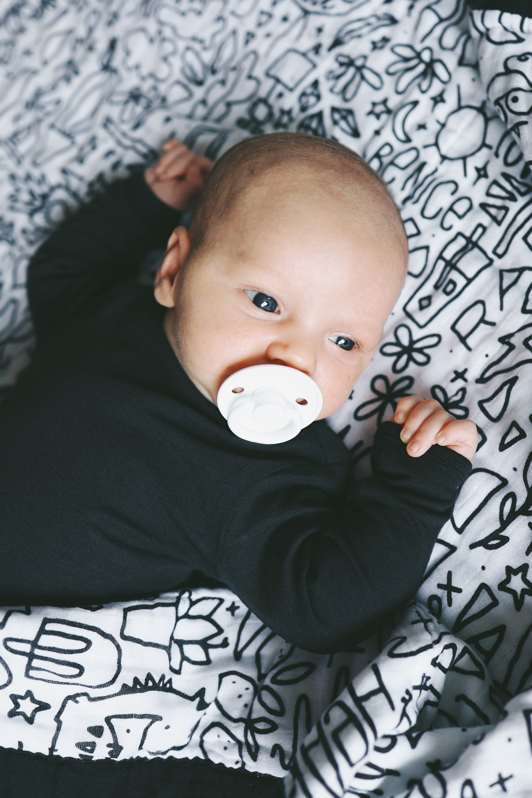 A baby with a binky laying on the quilt