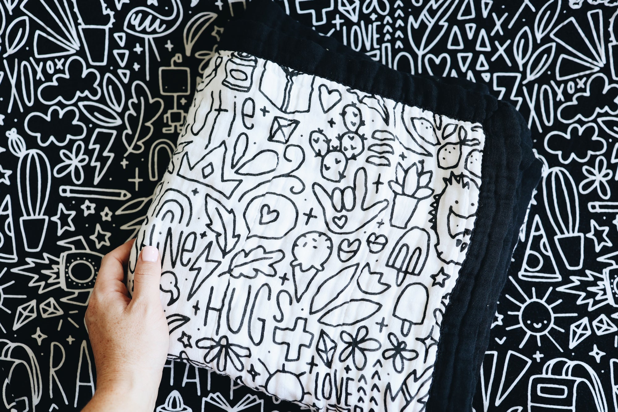 A hand holding the quilt folded in a square on a doodled background