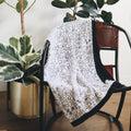 The quilt draped over a chair with houseplants in the background