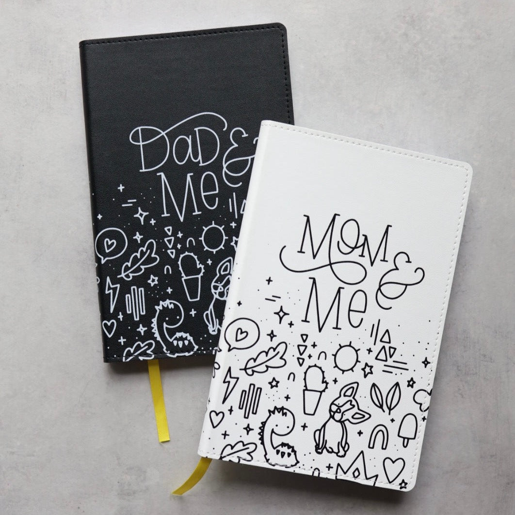 The mom &amp; me journal partially on top of the dad &amp; me journal on a desk