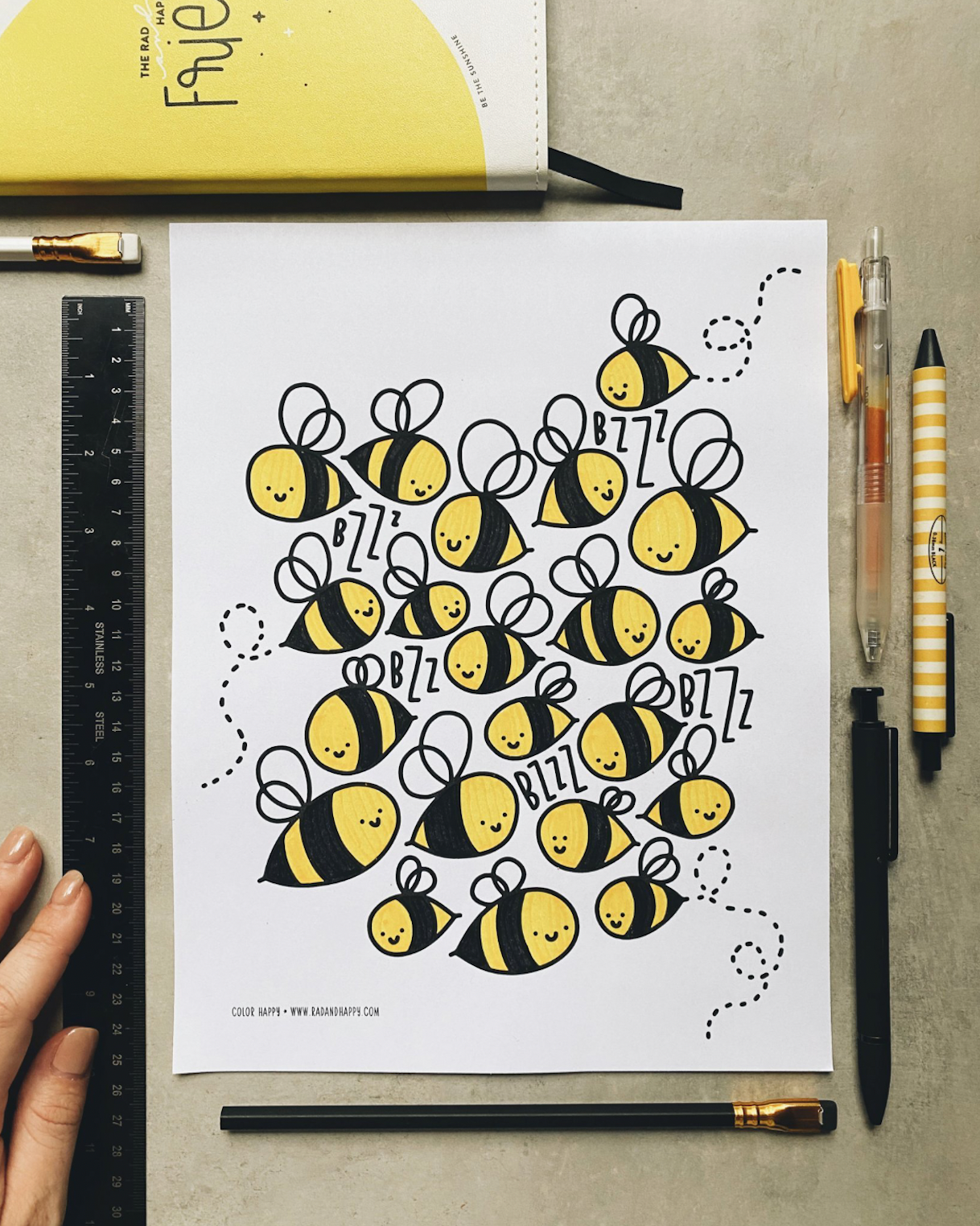 Sheet of paper with bee illustrations on a desk with stationery items.