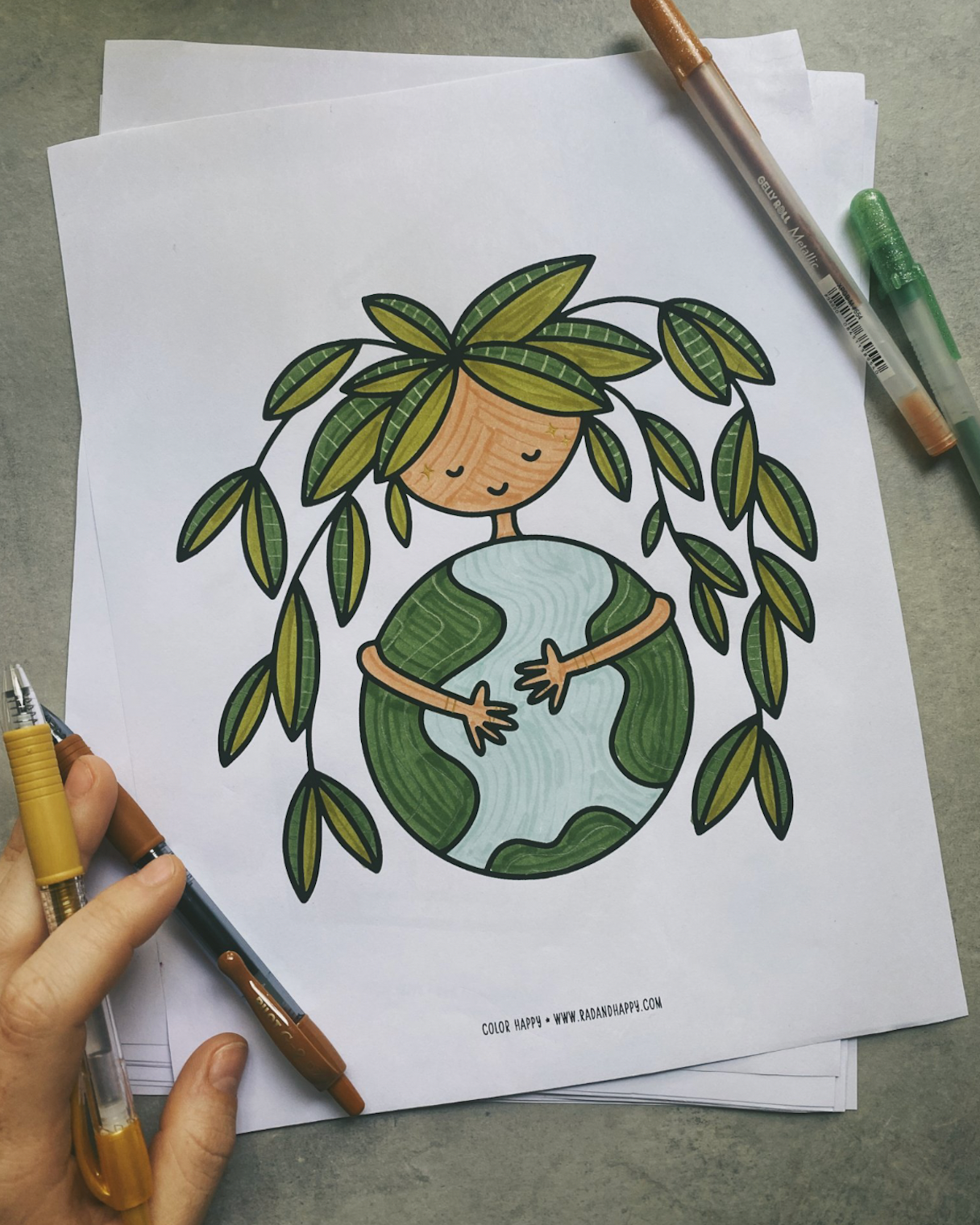Coloring page with a person holding the Earth surrounded by leaves, held by a hand with coloring tools.